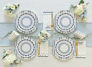 Set of decorative plates with floral arrangements and cutlery on a light blue tablecloth.
