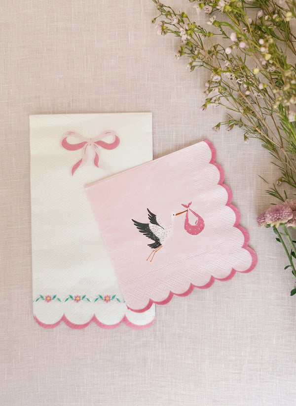 Pink embroidered card with scalloped edge and stork design on a textured surface with flowers.