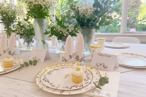 Easter table setting with bunny ears, flowers, and a cupcake.