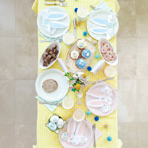Easter-themed table setting with pastel colors and bunny plates on a yellow checkered tablecloth.