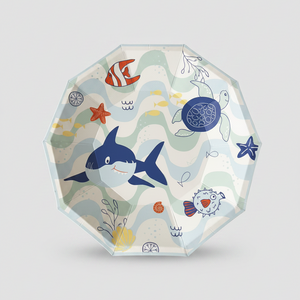 A clear octagonal plastic plate featuring a colorful cartoon ocean-themed print with a blue shark, red fish, sea turtle, starfish, and wavy lines on a light gray background.