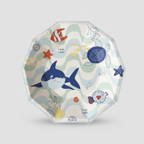 A clear octagonal plastic plate featuring a colorful cartoon ocean-themed print with a blue shark, red fish, sea turtle, starfish, and wavy lines on a light gray background.